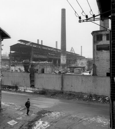 Czarno-biała fotografia Arkadiusza Goli wykonana w Bytomiu na terenie po byłej kopalni w Bobrku. Na pierwszym planie mężczyzna zbierający złom.