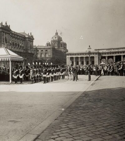 Fotografia w sepii. Na placu stoją żołnierze w eleganckich mundurach.