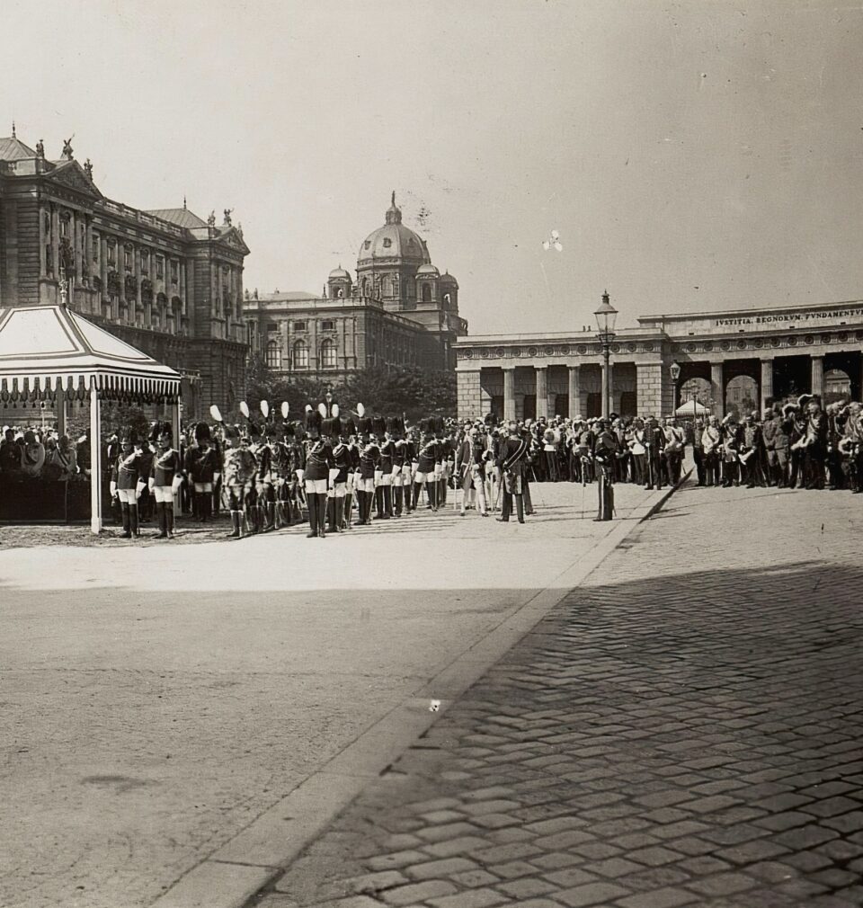 Fotografia w sepii. Na placu stoją żołnierze w eleganckich mundurach.